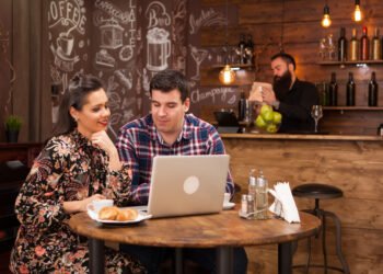 Wizytówka Google - Para pracuje przy laptopie w kawiarni, a w tle widać bar i obsługę – scenka związana z promocją lokalnego biznesu