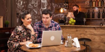 Wizytówka Google - Para pracuje przy laptopie w kawiarni, a w tle widać bar i obsługę – scenka związana z promocją lokalnego biznesu